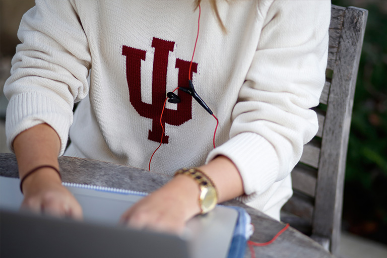 A person seated working on a laptop wearing a sweater with the IU trident. 